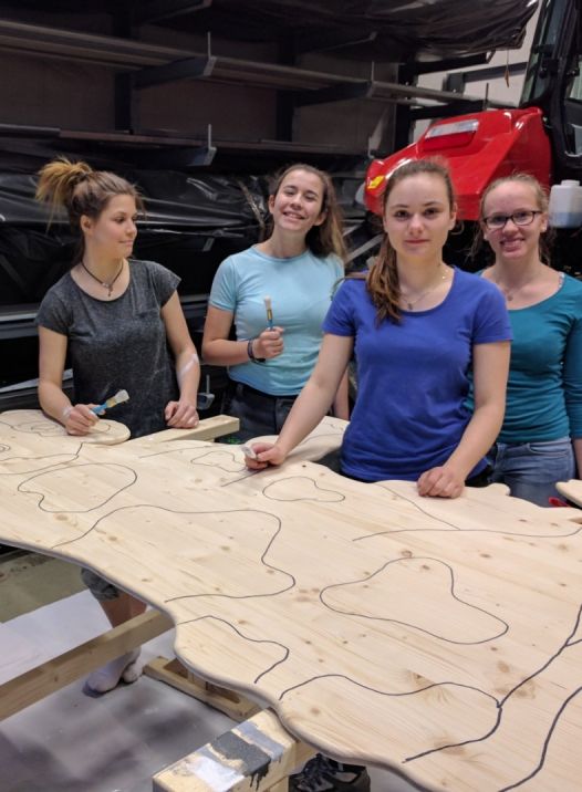 4 Mädchen beim Bearbeiten einer Holzplatte in einer Werkstatt