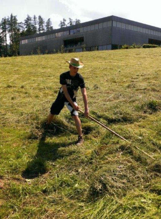 Junger Mann mit Strohhut rächt geschnittenes Gras